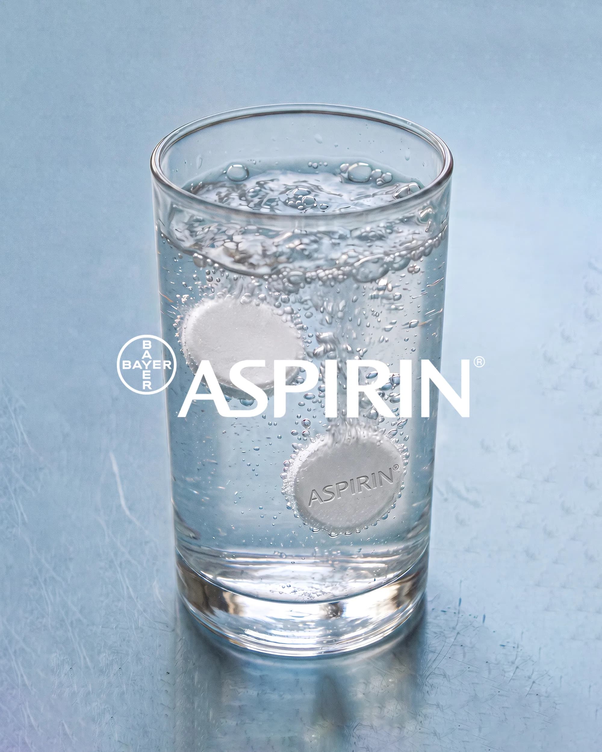 Aspirin-Tablette sprudelt in einem Glas Wasser, daneben das Aspirin-Logo